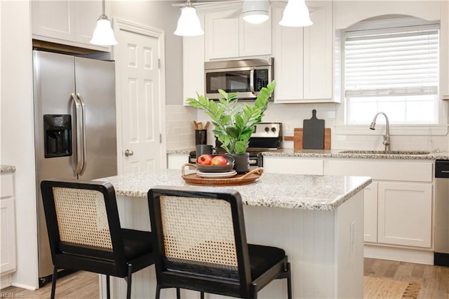 kitchen with a kitchen breakfast bar, backsplash, appliances with stainless steel finishes, a sink, and light wood finished floors