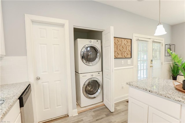 washroom featuring laundry area, light wood-type flooring, stacked washer and clothes dryer, and a wainscoted wall