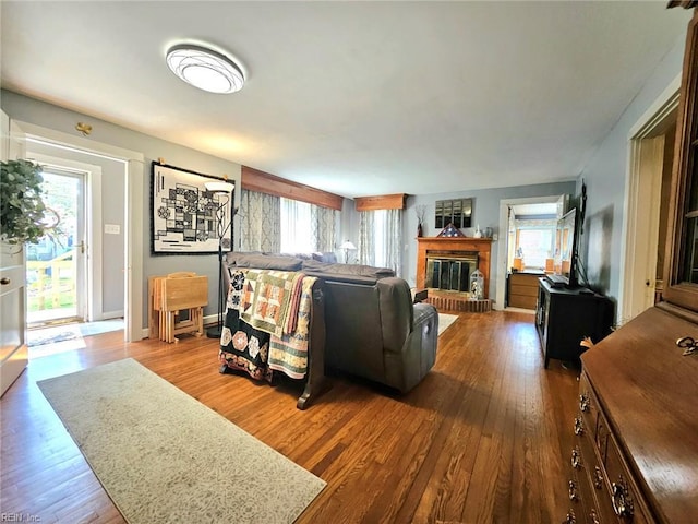 living area with a brick fireplace, baseboards, a wealth of natural light, and wood finished floors