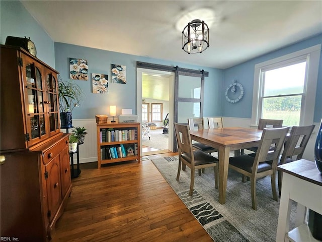 dining space with a barn door, dark wood-style floors, and a wainscoted wall