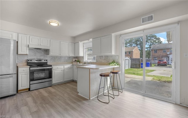kitchen with light wood finished floors, light countertops, stainless steel appliances, white cabinetry, and decorative backsplash