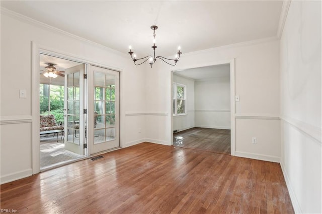 unfurnished dining area with an inviting chandelier, crown molding, visible vents, wood finished floors, and baseboards