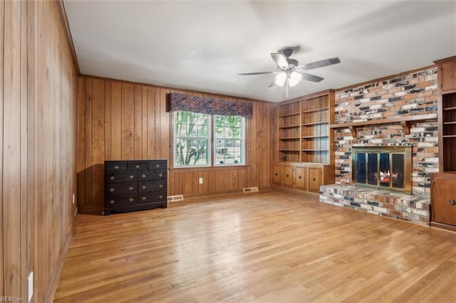 unfurnished living room with wooden walls, ceiling fan, wood finished floors, and visible vents