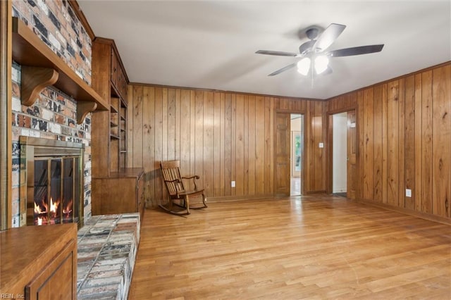sitting room with a ceiling fan, baseboards, wood walls, and light wood finished floors