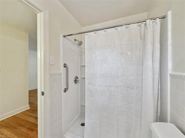 bathroom with tile walls, toilet, wood finished floors, and a shower with shower curtain
