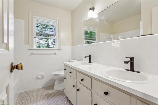 full bath with a sink, tile walls, toilet, and double vanity