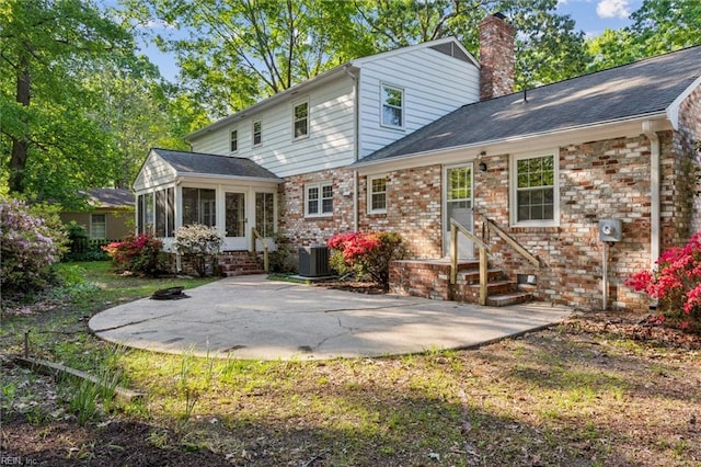 rear view of property with brick siding, a sunroom, entry steps, a chimney, and a patio