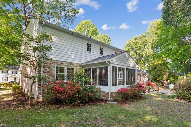 rear view of house with a yard, a sunroom, and brick siding