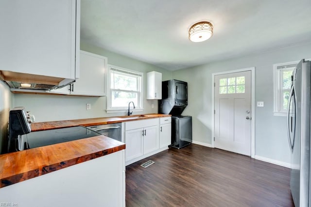 kitchen featuring butcher block counters, a healthy amount of sunlight, a sink, stacked washer / drying machine, and stainless steel appliances