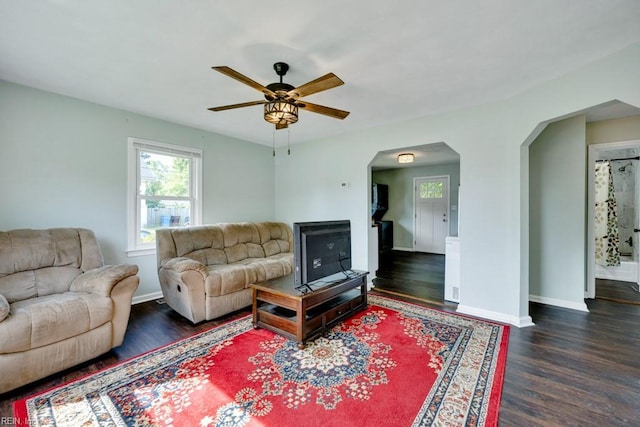 living room with baseboards, arched walkways, dark wood finished floors, and ceiling fan