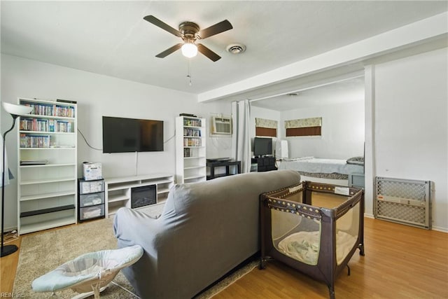 living room with ceiling fan, visible vents, a wall unit AC, and wood finished floors