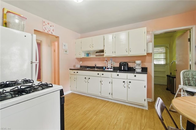 kitchen with dark countertops, a sink, white appliances, white cabinetry, and light wood-type flooring