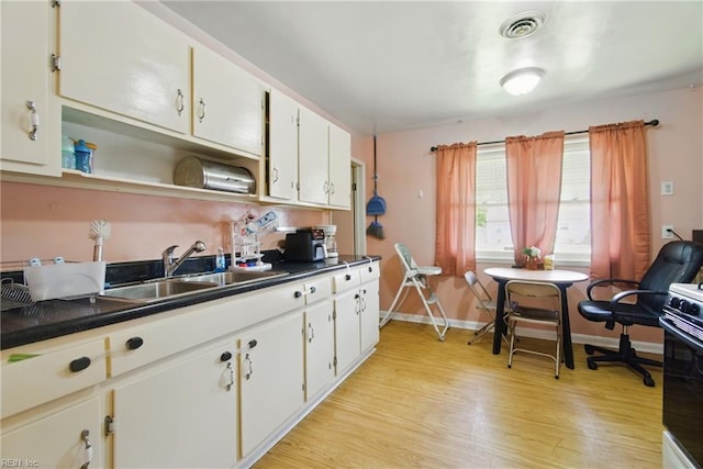 kitchen featuring visible vents, dark countertops, light wood-style floors, baseboards, and a sink