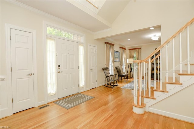 foyer entrance with visible vents, crown molding, light wood-type flooring, baseboards, and stairs
