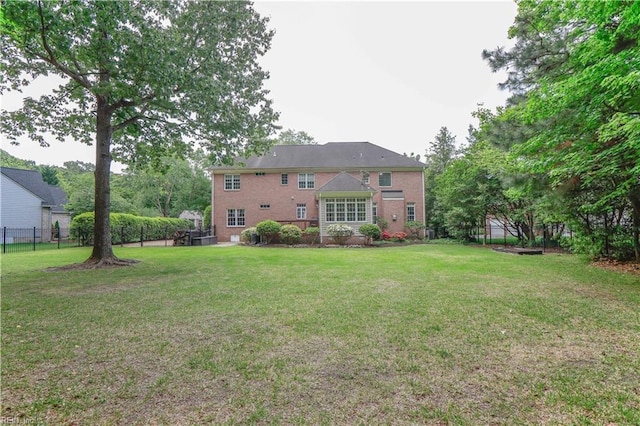rear view of property featuring a lawn, brick siding, and fence