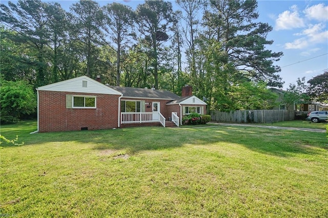 back of property with brick siding, a lawn, fence, and crawl space