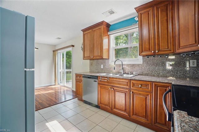kitchen with brown cabinets, a sink, freestanding refrigerator, stainless steel dishwasher, and visible vents