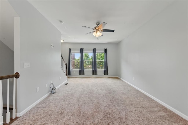 spare room with ceiling fan, carpet, baseboards, visible vents, and stairway