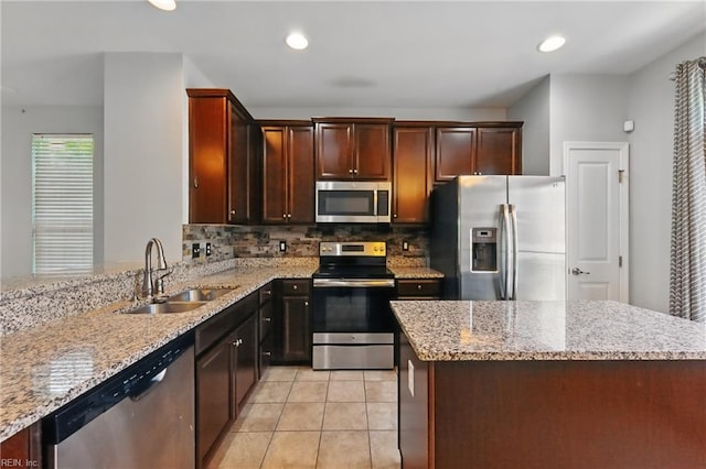 kitchen featuring light stone counters, a sink, stainless steel appliances, decorative backsplash, and light tile patterned floors