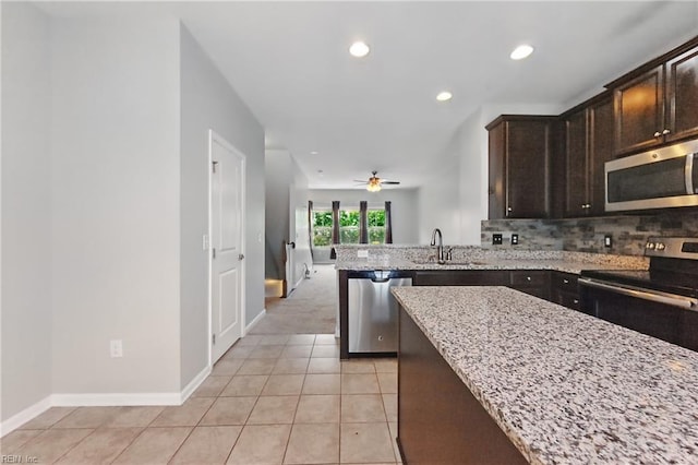 kitchen featuring dark brown cabinetry, appliances with stainless steel finishes, a sink, light stone counters, and recessed lighting