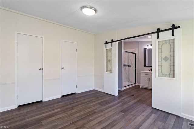 unfurnished bedroom with dark wood-style floors, a barn door, and a sink