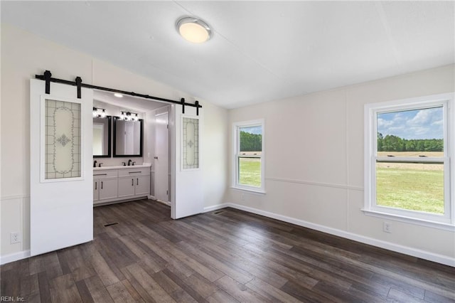 unfurnished bedroom featuring vaulted ceiling, a barn door, baseboards, ensuite bathroom, and dark wood-type flooring