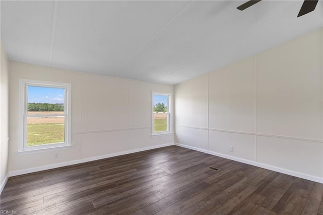 unfurnished room featuring a ceiling fan, baseboards, dark wood finished floors, and a decorative wall