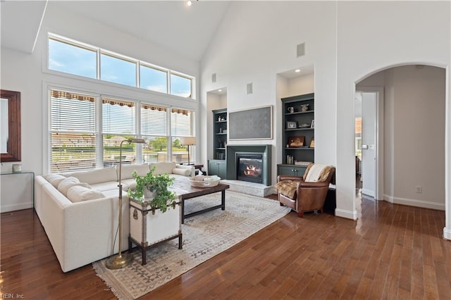 living room featuring dark wood-style flooring, arched walkways, baseboards, and a glass covered fireplace