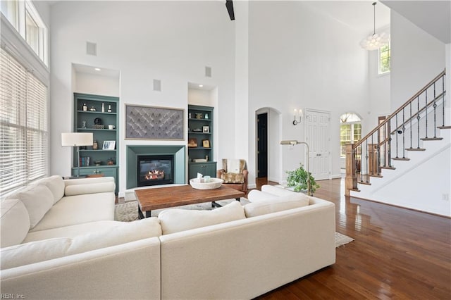 living room with arched walkways, a high ceiling, plenty of natural light, and dark wood-type flooring