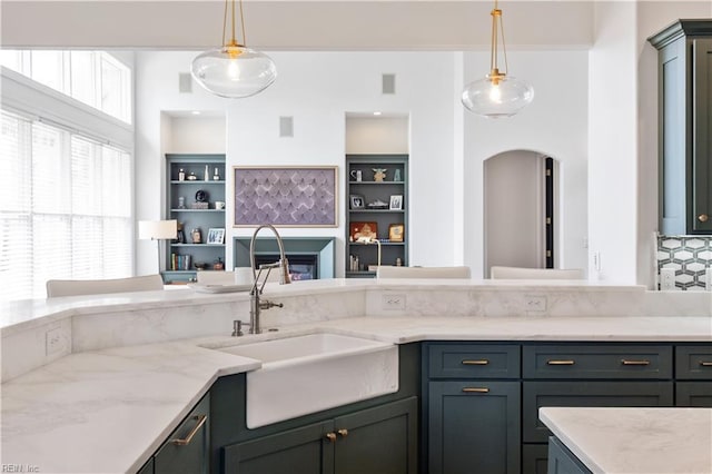 kitchen with light stone counters, a sink, arched walkways, and decorative light fixtures