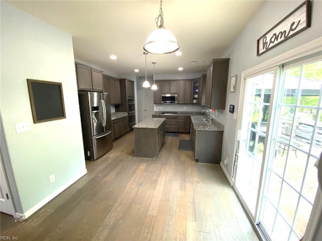kitchen featuring appliances with stainless steel finishes, a sink, light wood-style floors, baseboards, and a kitchen island