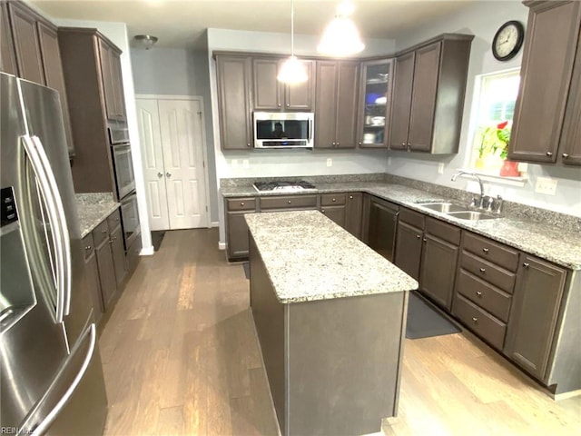 kitchen with light stone countertops, a sink, a center island, stainless steel appliances, and wood finished floors