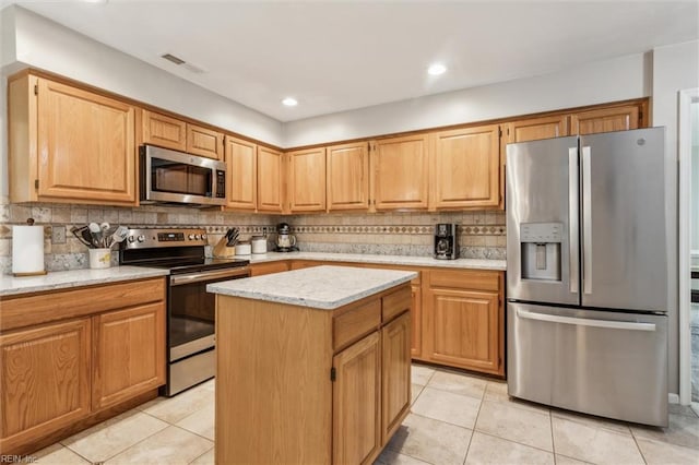 kitchen featuring light tile patterned flooring, light stone counters, stainless steel appliances, tasteful backsplash, and a kitchen island
