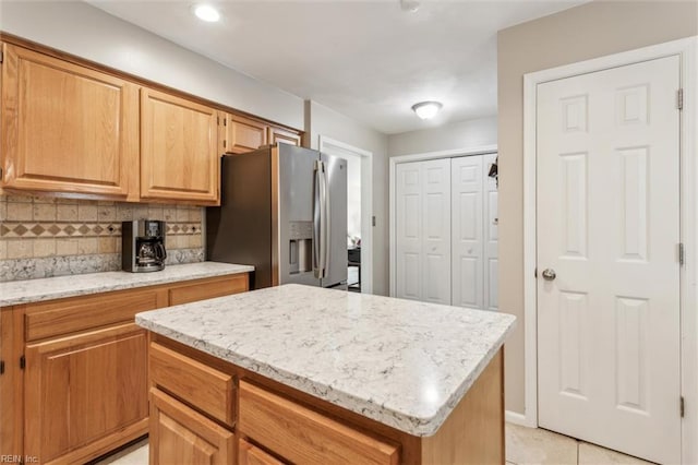 kitchen with a kitchen island, light stone countertops, decorative backsplash, and stainless steel fridge with ice dispenser