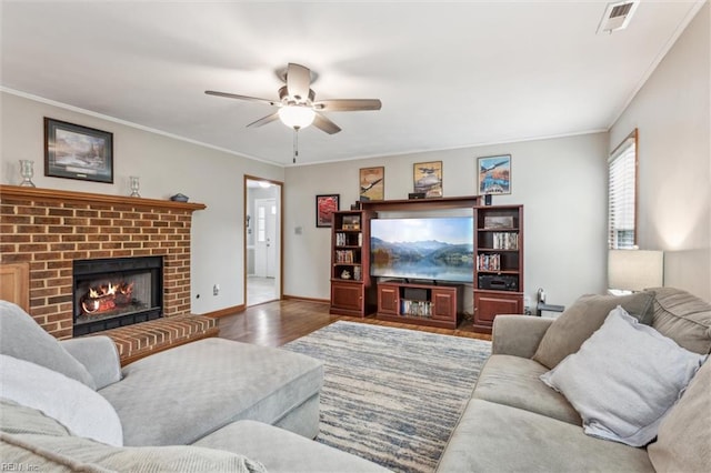 living area with a ceiling fan, a fireplace, wood finished floors, baseboards, and ornamental molding