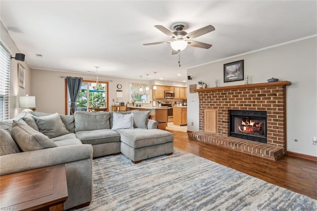 living area with ornamental molding, a brick fireplace, ceiling fan, and wood finished floors