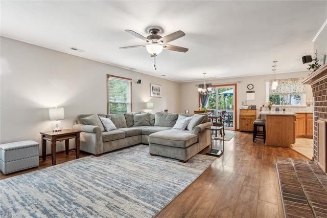living room featuring wood-type flooring, visible vents, and ceiling fan with notable chandelier