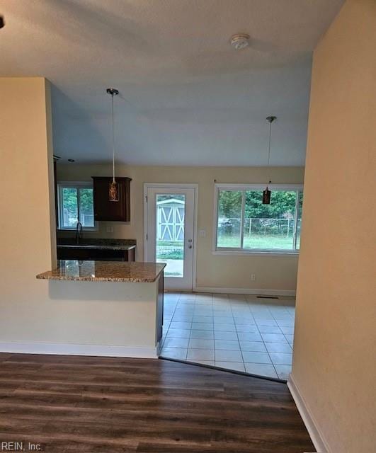 kitchen featuring pendant lighting, baseboards, stone countertops, and wood finished floors