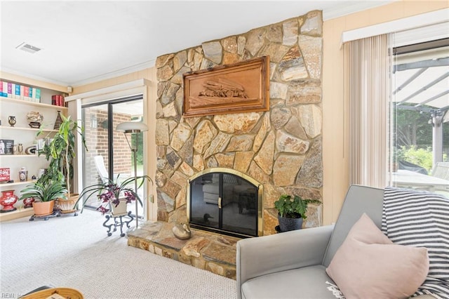 carpeted living area with a stone fireplace, ornamental molding, and visible vents