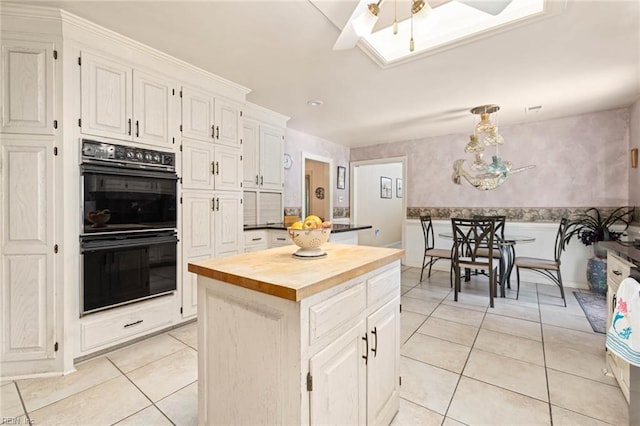 kitchen with dobule oven black, a kitchen island, a skylight, light tile patterned floors, and wood counters