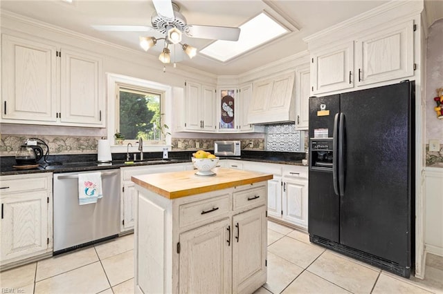 kitchen with stainless steel dishwasher, a sink, wood counters, black fridge, and light tile patterned flooring