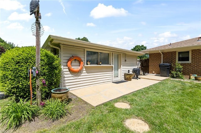 back of property featuring a lawn, a patio, and brick siding