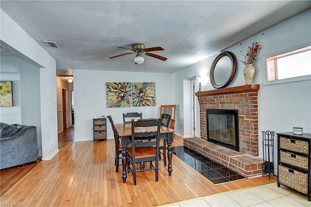 dining room with wood-type flooring, a ceiling fan, a brick fireplace, and visible vents