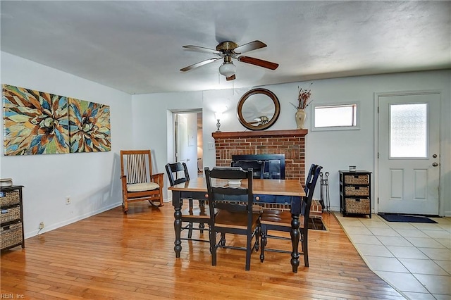 dining area with a fireplace, ceiling fan, baseboards, and light wood-type flooring