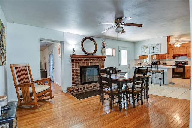 dining space with a brick fireplace, a ceiling fan, and light wood-type flooring