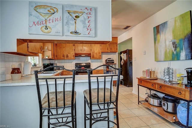 kitchen featuring brown cabinets, backsplash, black fridge, and electric stove