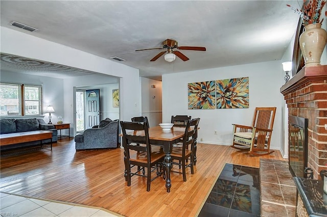 dining room with a fireplace, a ceiling fan, hardwood / wood-style flooring, and visible vents
