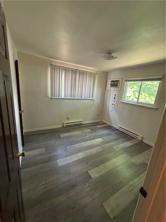 spare room featuring an AC wall unit, a baseboard radiator, baseboards, and wood finished floors
