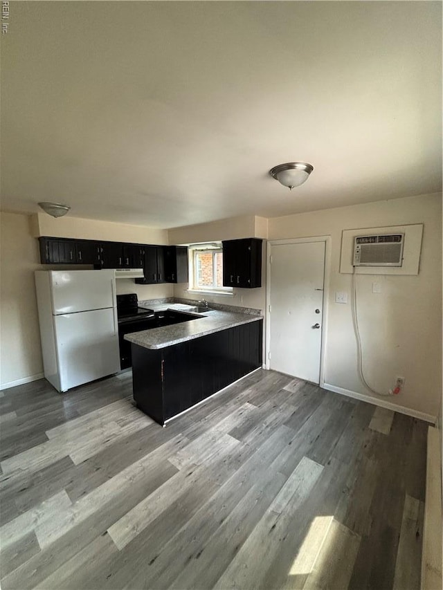 kitchen featuring freestanding refrigerator, an AC wall unit, a peninsula, dark cabinetry, and light wood-style flooring