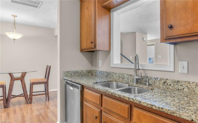 kitchen featuring stainless steel dishwasher, visible vents, light wood-type flooring, brown cabinets, and a sink
